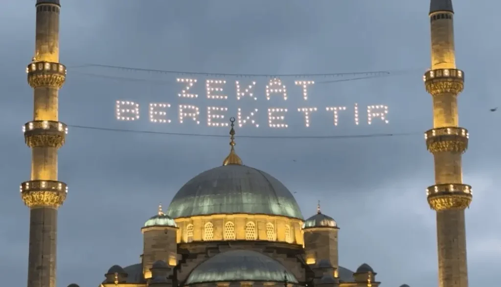 Di antara dua menara megah Masjid Yeni di Istanbul, Turki, tulisan bercahaya mahya menampilkan pesan: “Zakat membawa berkah,” pada penghujung Ramadan tahun ini.(Foto: Ivory)
